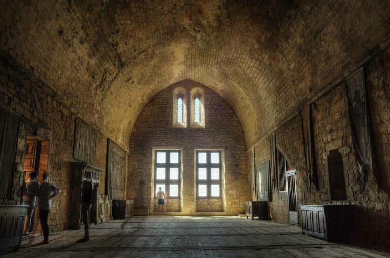 Visitors exploring the rustic and historical interior of Chateau de Beynac, featuring arched ceilings and medieval stone architecture in France.