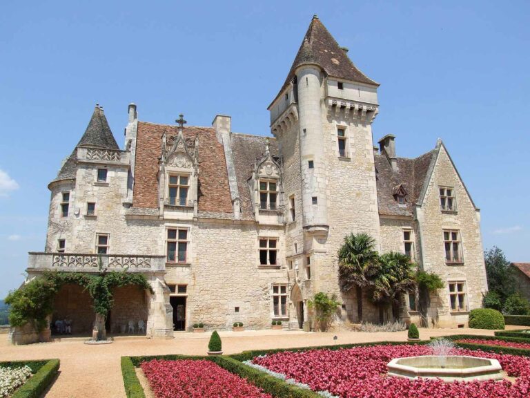 Chateau des Milandes, a historical French castle with ornate stone facade, lush garden, and central fountain in France's Dordogne region.