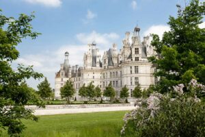 Spring view of Château de Chambord with blooming flowers and lush greenery, a major tourist attraction in Chambord, France.