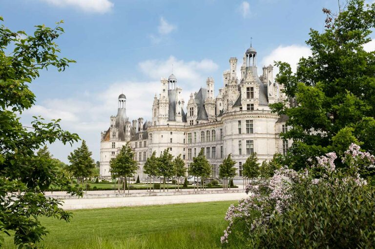 Spring view of Château de Chambord with blooming flowers and lush greenery, a major tourist attraction in Chambord, France.