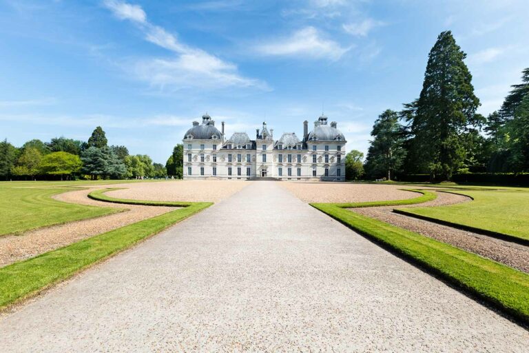 Symmetrical view of Château de Cheverny in Cheverny, France, showcasing its classical French architecture, manicured gardens, and grand gravel pathway under a clear blue sky.