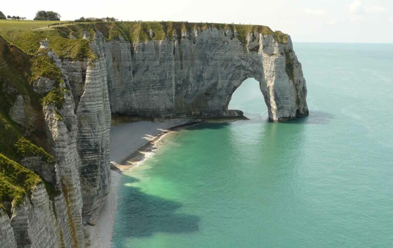 Breathtaking view of the limestone cliffs of Etretat with natural arch and turquoise waters in Normandy, France, highlighting coastal erosion and natural beauty.