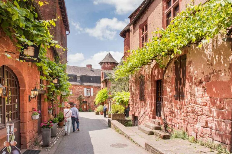Tourists walking through the picturesque village of Collonges-la-Rouge, France, featuring unique red sandstone buildings and vine-covered streets.