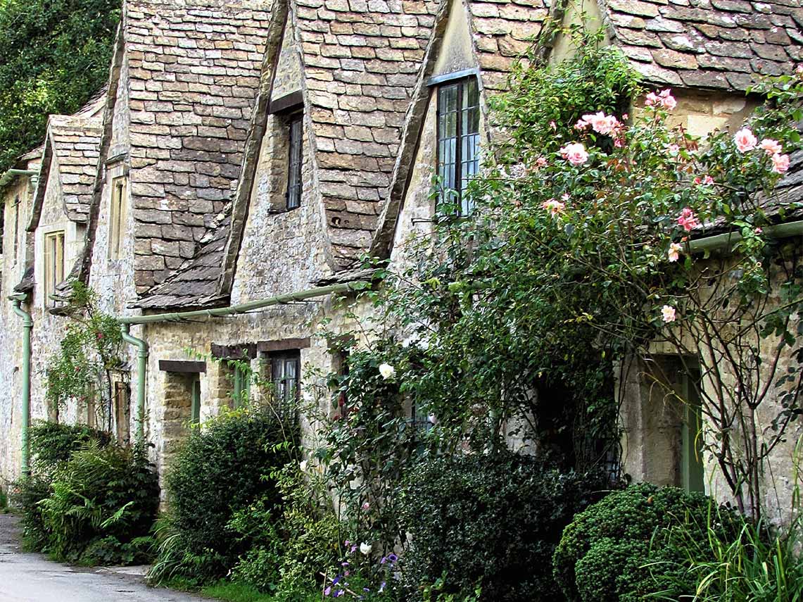 Traditional Cotswold stone cottages with climbing roses and lush greenery in a quaint English village.