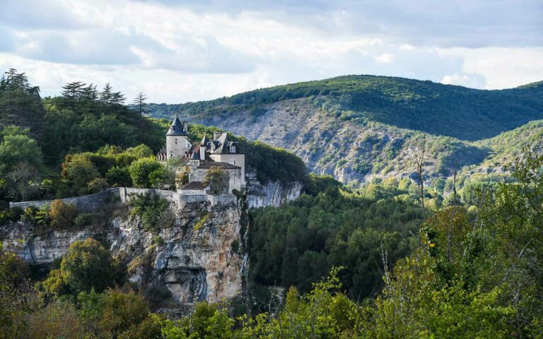 French Cliff Chateaux perched on a rocky ledge overlooking lush green forests in France, an iconic tourist attraction for historical tours.