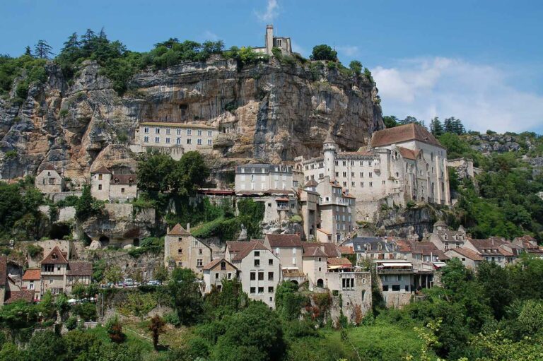 Scenic view of Rocamadour, a historic pilgrimage site built on a cliff in France, showcasing medieval buildings and lush greenery.