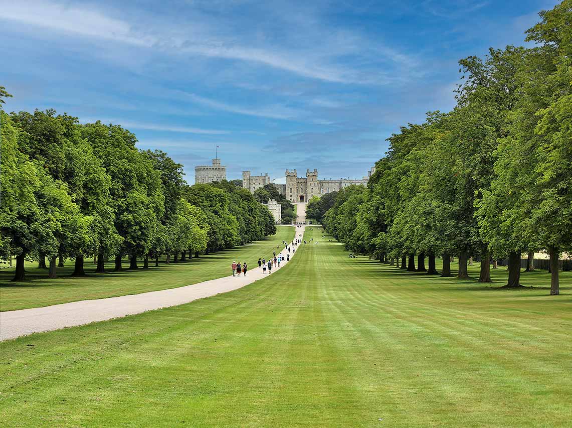 Visitors walking along a lush green path towards Windsor Castle in England under a clear blue sky