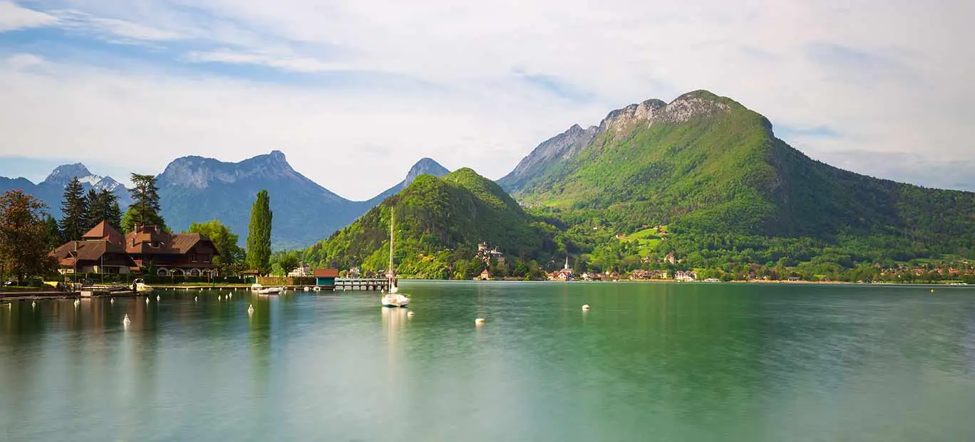 Yacht in the harbour overlooked by mountain range in the French Alps.
