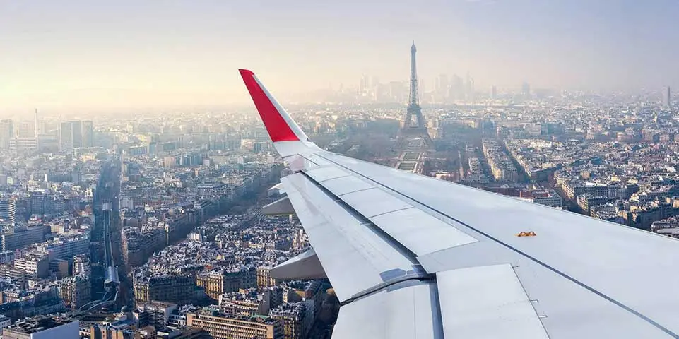 view over the wing of a plane flying over Paris with Eiffel tower in background.