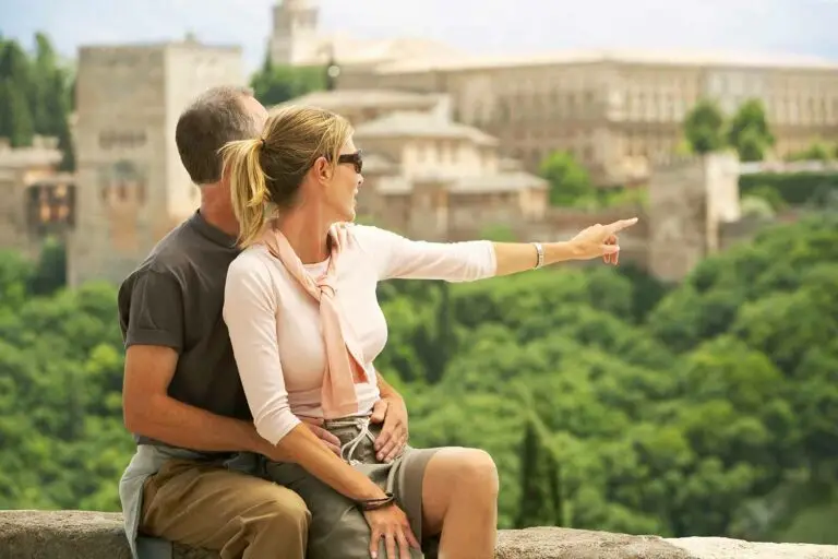 Middle aged couple sitting on wall with woman pointing at view