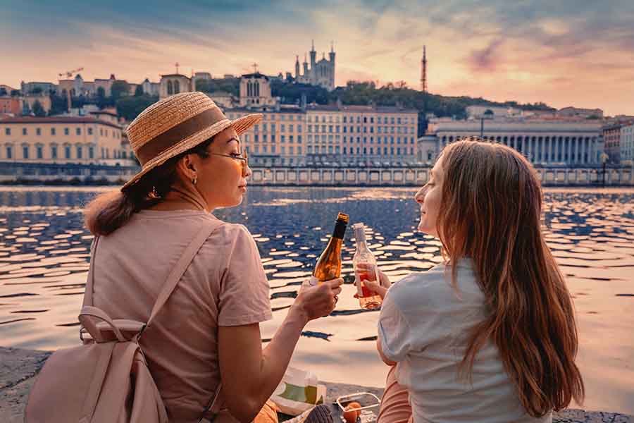 two female tourists clinking wine bottles together in celebration in Lyon, France.