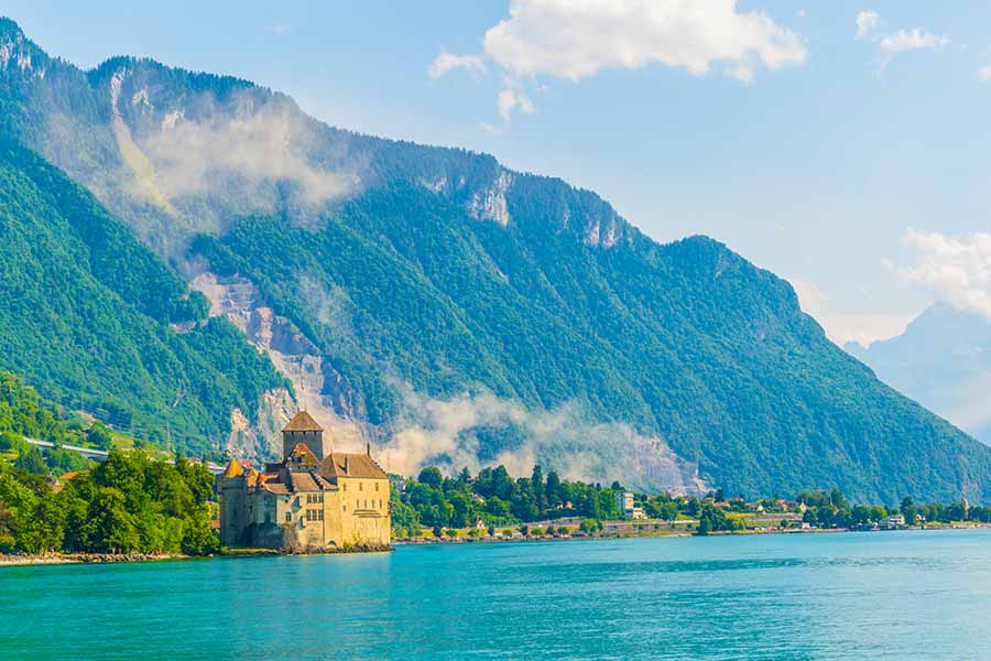 Scenic view of Chillon Castle on Lake Geneva with misty mountains in the background, Switzerland