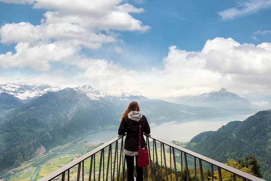 Woman observing the panoramic view of Interlaken and Swiss Alps from an elevated viewpoint, highlighting the serene beauty of Switzerland's landscapes for tourists.