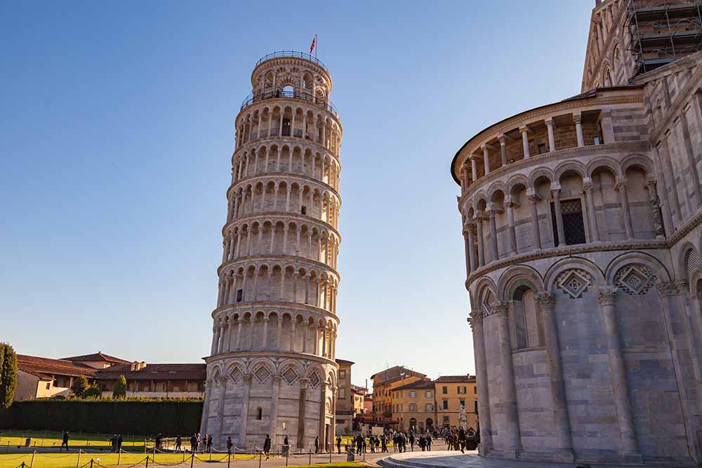 Leaning Tower of Pisa in Italy, iconic medieval architecture under clear blue skies, popular tourist attraction with visitors around the base