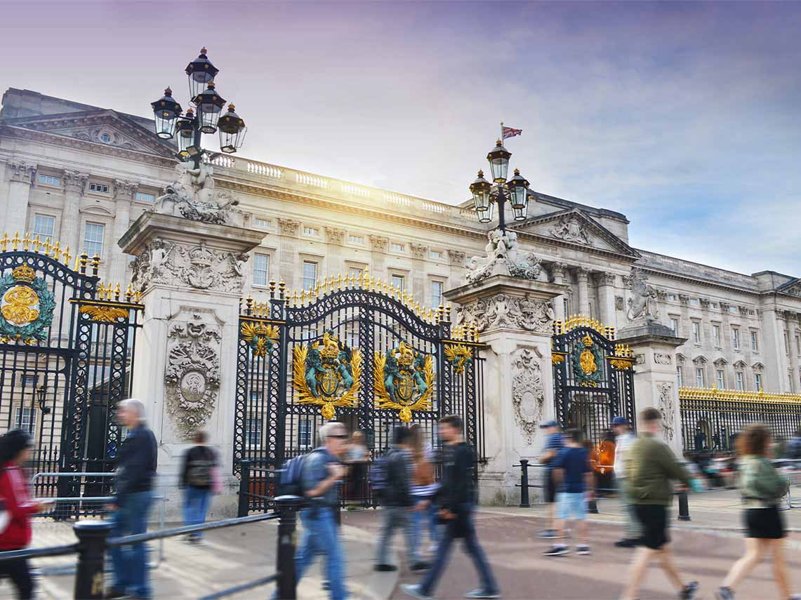 Tourists walking in front of the ornate gates of Buckingham Palace, London on a sunny day