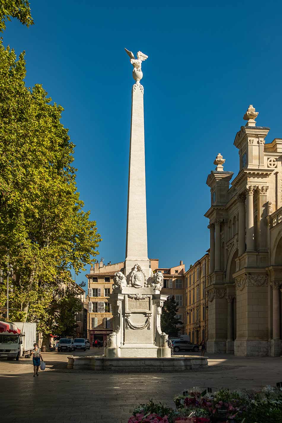 Historic monument at Place des Prêcheurs in Aix-en-Provence, France, featuring a tall white obelisk with sculptural details under a clear blue sky.