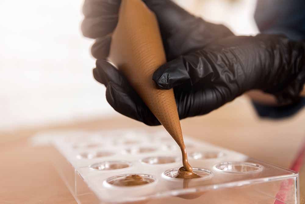 Person pouring melted chocolate into a mold during a chocolate making class in Belgium for a culinary tourism experience.