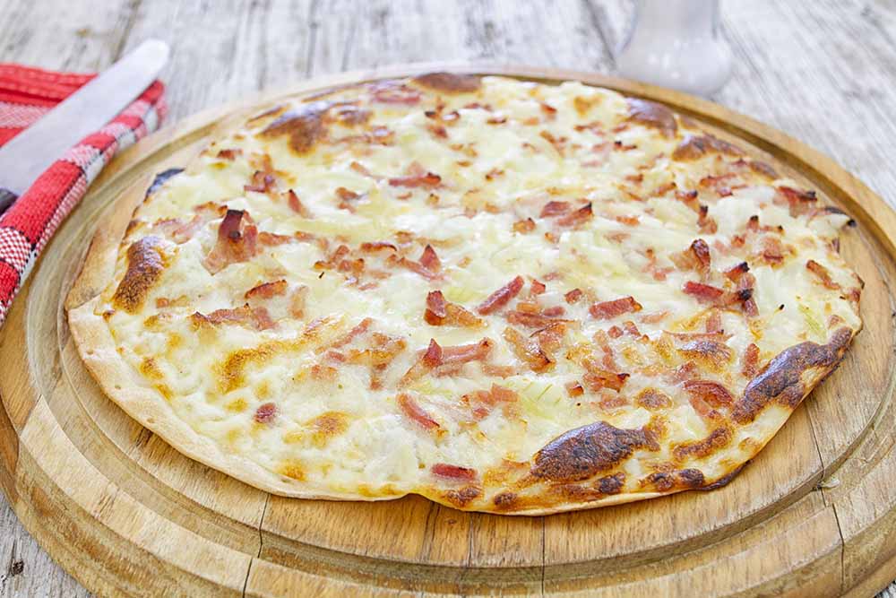 Traditional Flammkuchen served on a wooden board, a popular Alsace region dish in France, featuring crispy crust topped with cream, onions, and bacon.