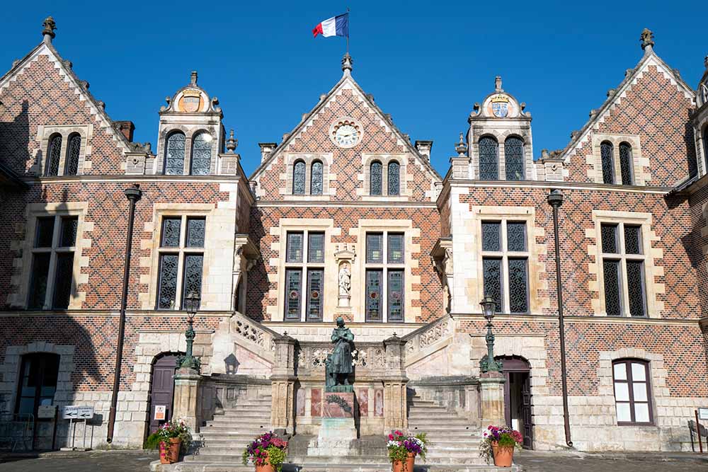 Front view of Hôtel Groslot in Orleans, France, showcasing the ornate Renaissance architecture with a statue at the entrance and the French flag flying atop.